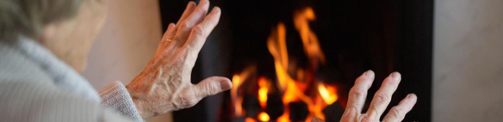 Picture of an old lady warming her hands by the fireside
